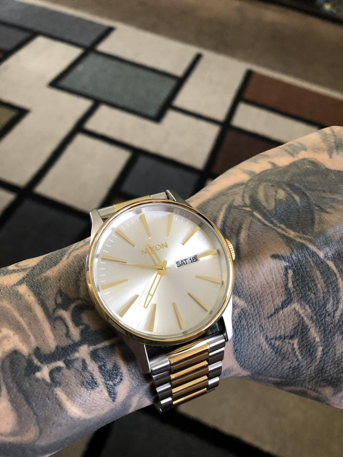 A gold and silver Nixon Sentry Stainless Steel quartz watch on a mans wrist