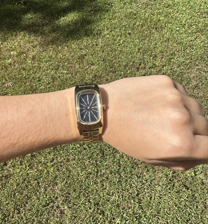 Gold wristwatch on a wrist with grass in the background
