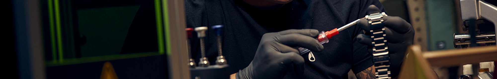 A person wearing black gloves uses a small screwdriver to work on a metal watch band.