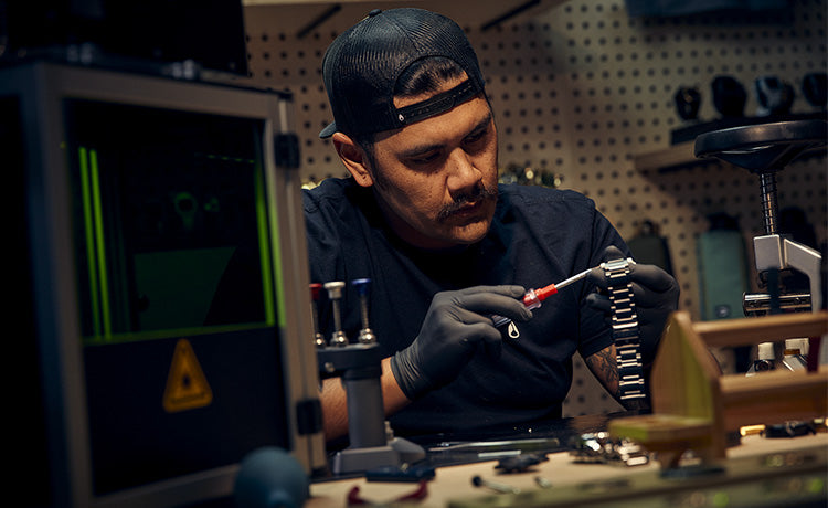 Technician in black gloves using a screwdriver to change a watch battery.