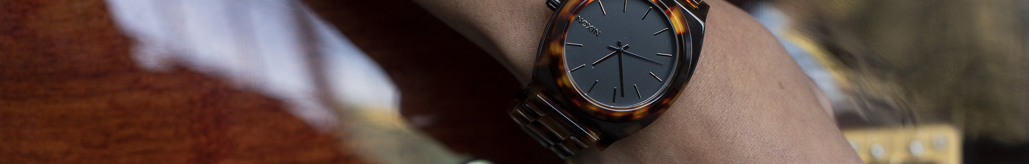 Close-up of a person's wrist wearing a quartz watch with a dark face and tortoiseshell-patterned band.