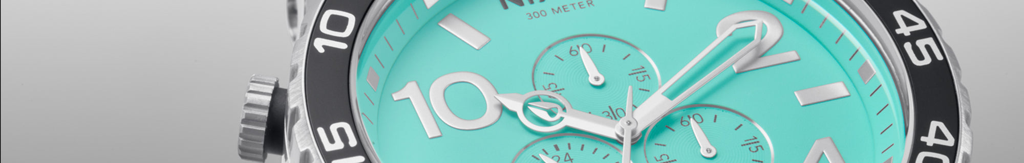 Close-up of a watch with a turquoise dial, silver markers, and a black bezel.