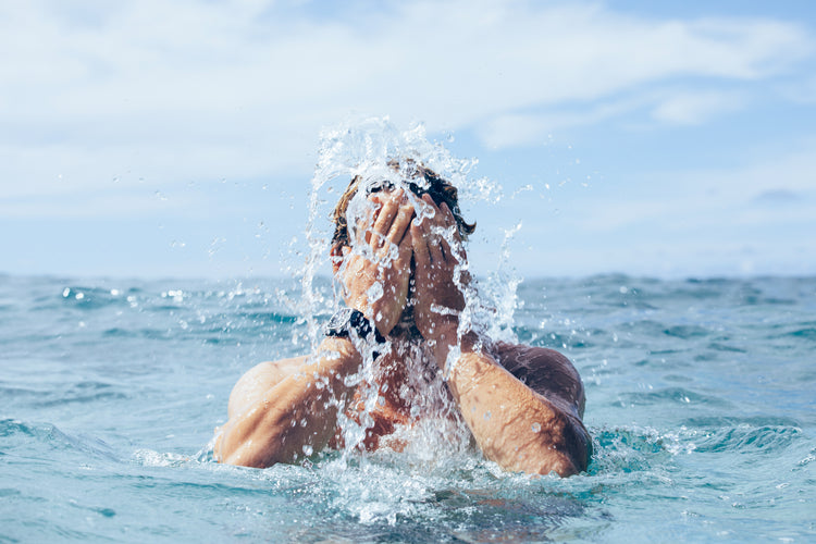 Surfer splashes his face in the ocean while wearing a Nixon watch
