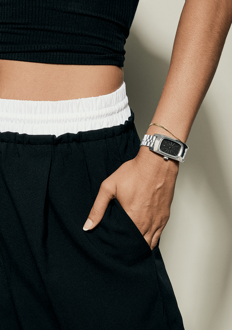 Woman wearing the Nixon Frankie analog watch in silver with a hand in her pocket.
