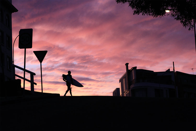 Surfer carrying a surfboard against a colorful sunset sky