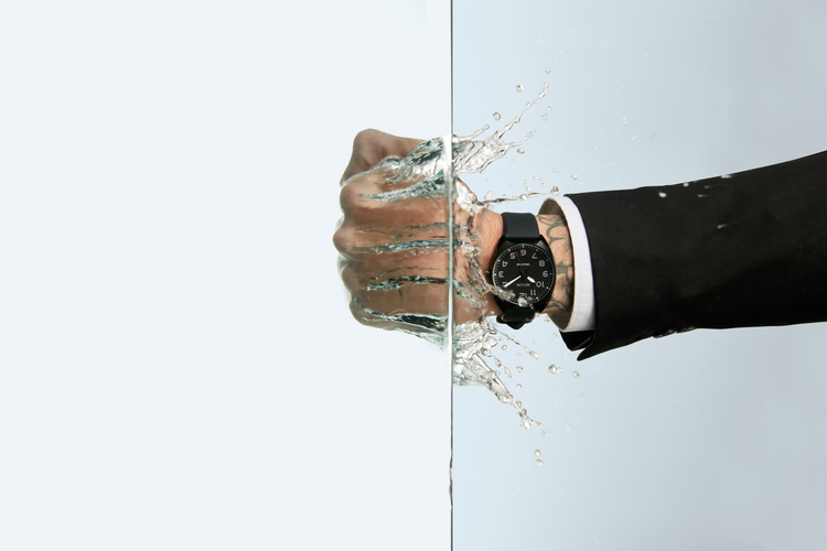 Man with a Nixon Mullet rubber strap watch putting his hand into water