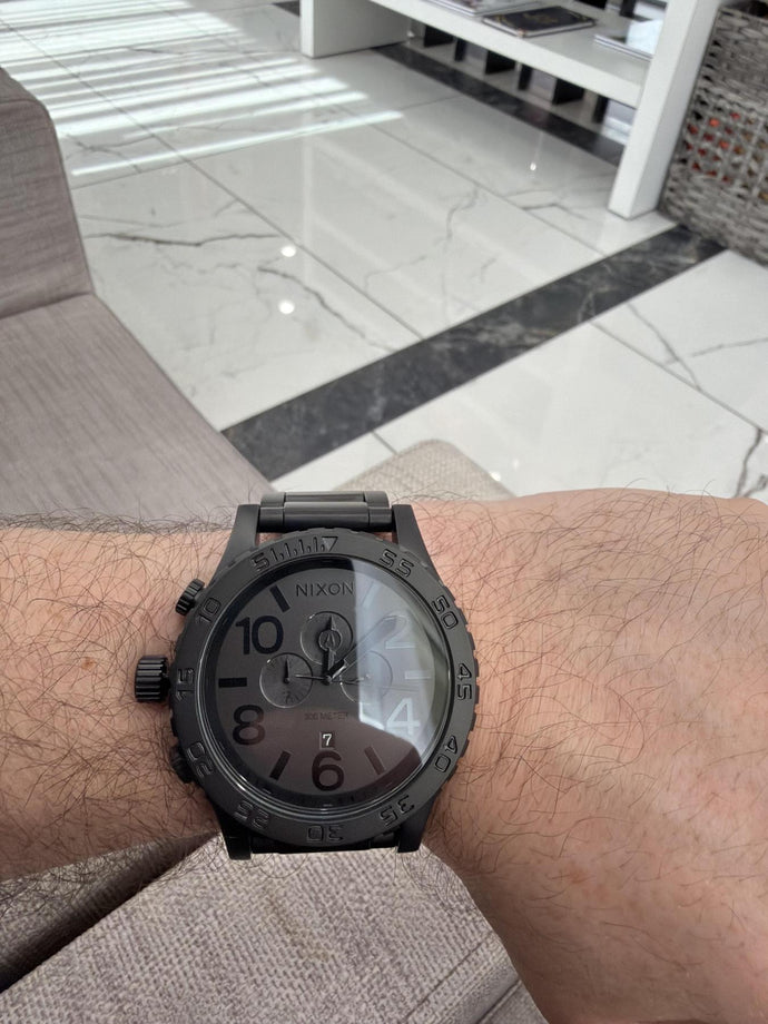 Man showing off his black Nixon 51-30 Chrono watch against a marble floor backdrop