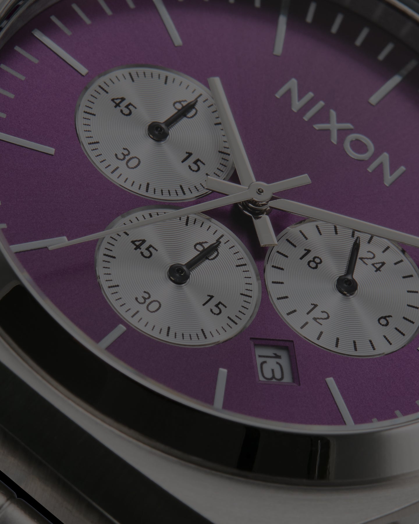 Close-up of a Nixon chronograph watch with a purple dial, silver-tone case, and three white subdials.