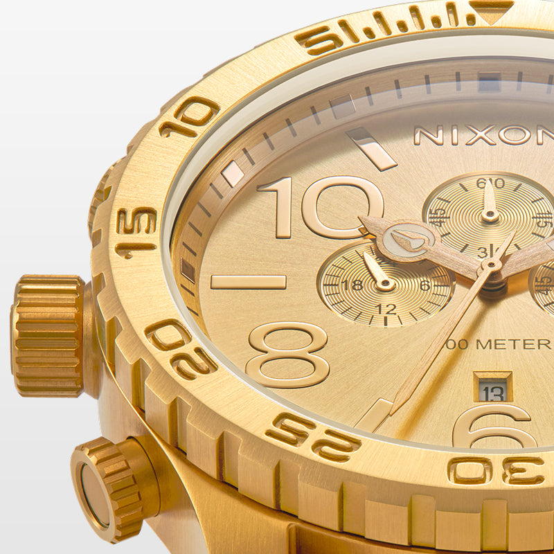 Close-up of a gold Nixon chronograph watch with a brushed finish, showing the watch face, subdials, and bezel.