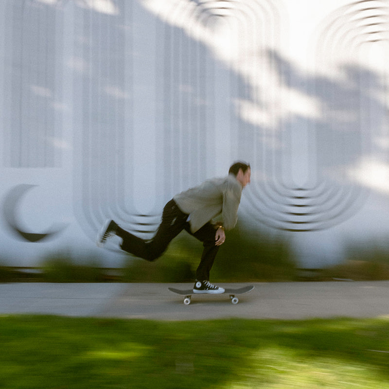 Dynamic shot of a man skateboarding past a white wall with abstract designs.