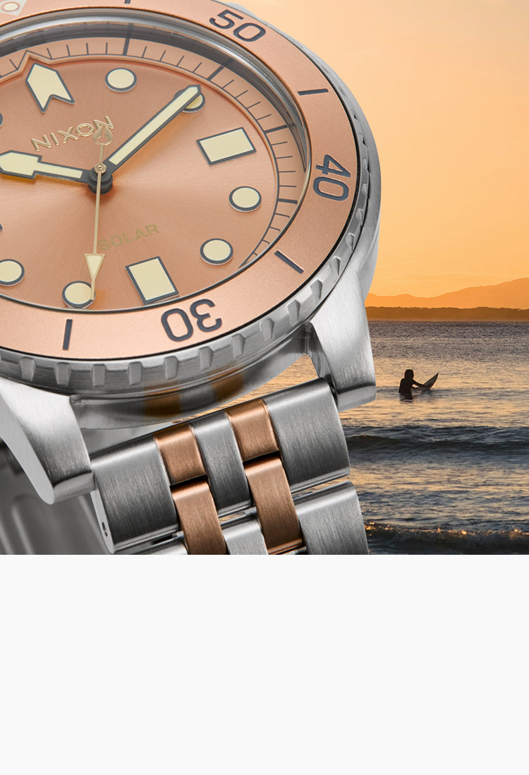 rose gold and silver watch over a ocean and surfer photo