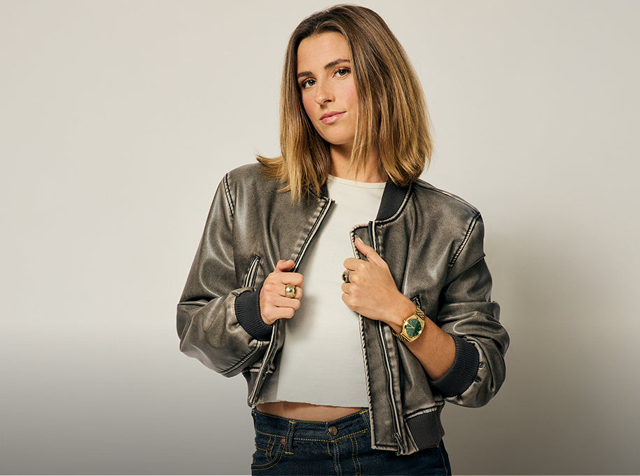 Woman wearing a jacket and posing with the gold Nixon Time Teller analog watch for women