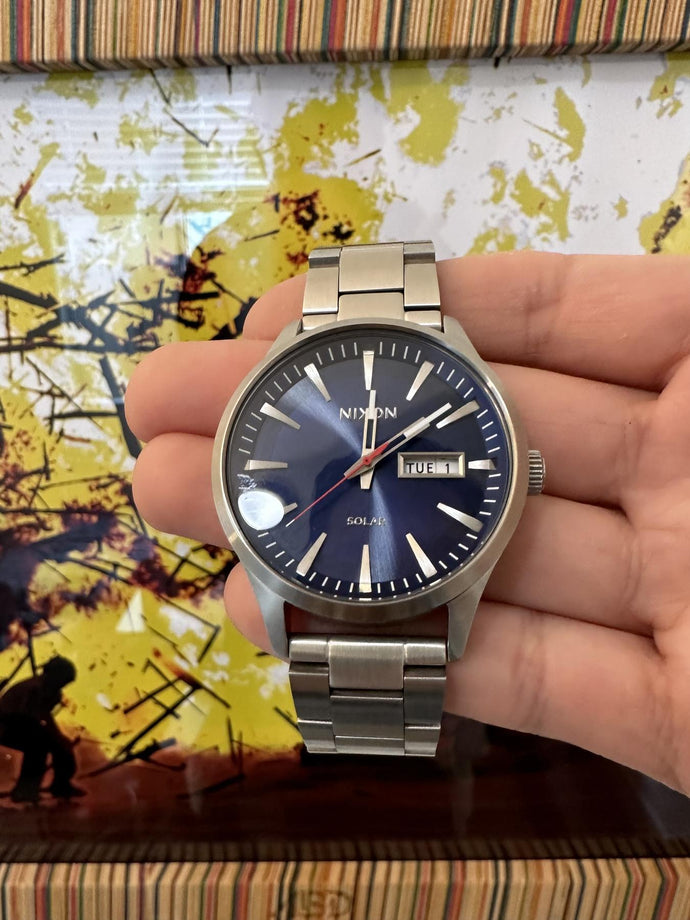 Person showing off their blue Nixon Sentry Solar Stainless Steel in front of an art wall