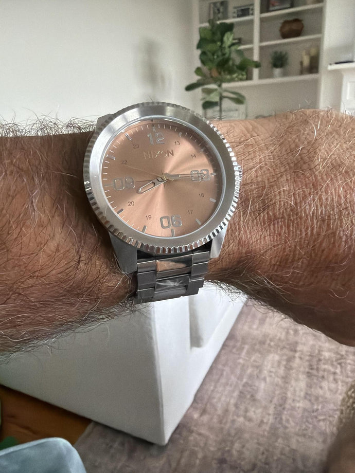 Man in his home holds his wrist up to show off the Corporal Stainless Steel in Silver / Coral.