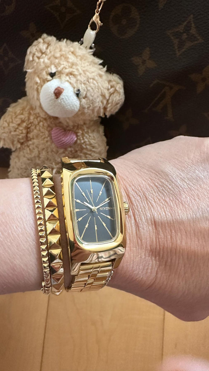 Woman in front of a teddy bear shows of a gold Nixon Frankie analog watch.