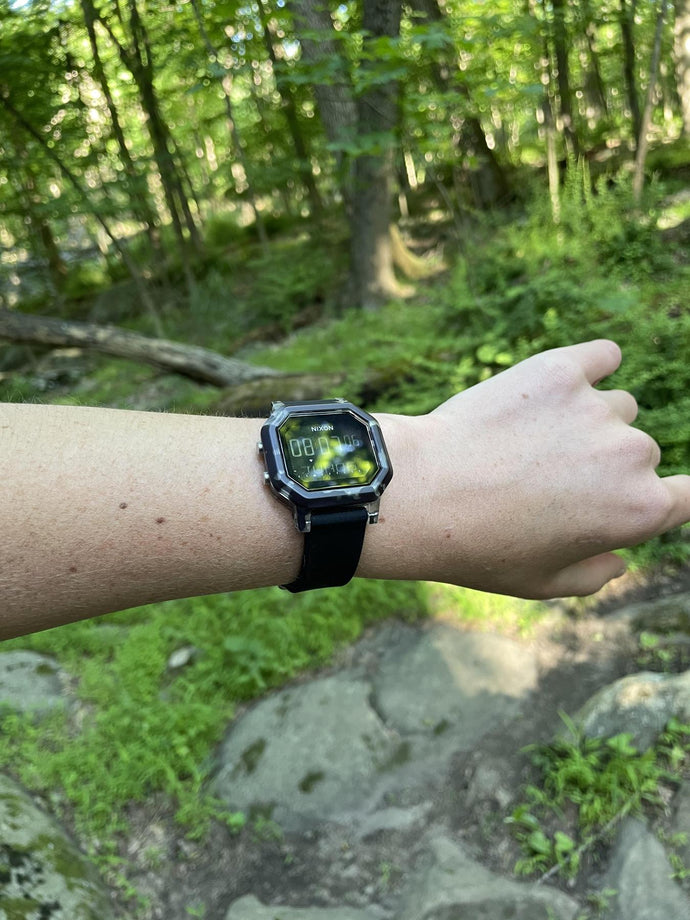 Woman in the outdoors holds her wrist up to show her Black Tortoise Nixon Siren digital watch.